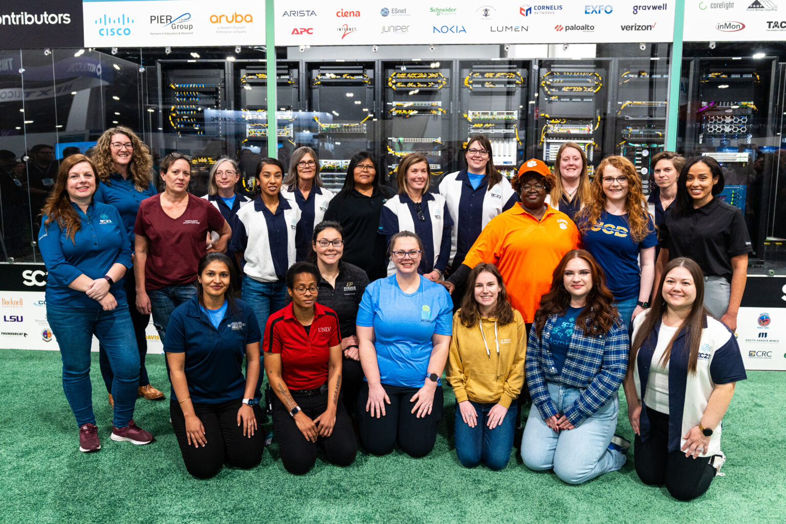 A group of women, including Sawadogo, stand in front of supercomputing clusters at the Denver Supercomputing Conference in 2023